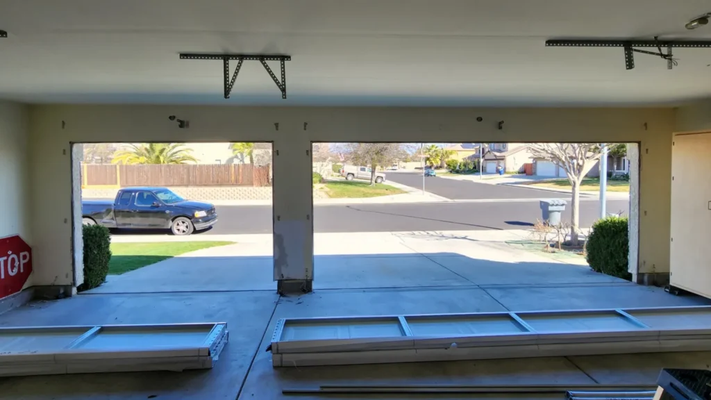 Open garage with frame parts on the floor and view of suburban street, trees, and parked vehicles outside.
