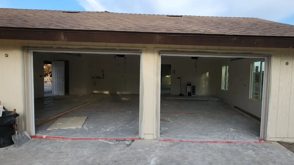 Empty double garage with open doors, under renovation with plastic covers on the floor.