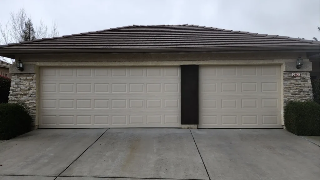 Suburban house with double garage doors and concrete driveway on a cloudy day.