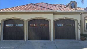 Three-car garage with wooden doors and a copper roof on a modern beige house.