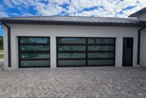 Modern garage with glass doors and a light brick driveway under a partly cloudy sky.