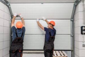 Two workers in safety gear installing a garage door inside a garage.